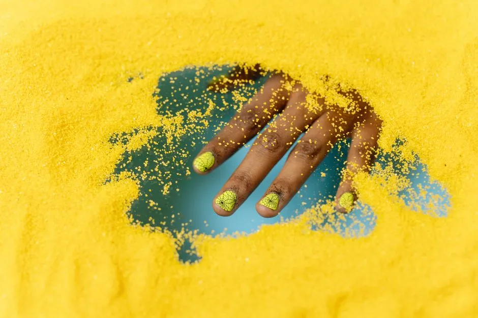 Hand med glitter naglar och dekorationer mot gul bakgrund